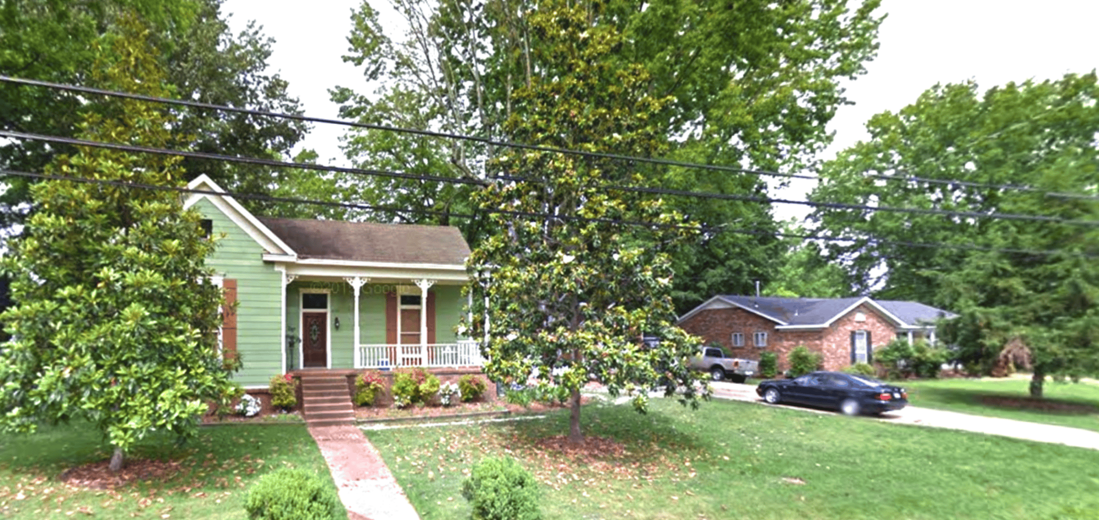 Quaint green historic house with porch, surrounded by lush trees and well-maintained lawn in Memphis, highlighting community charm and local heritage.
