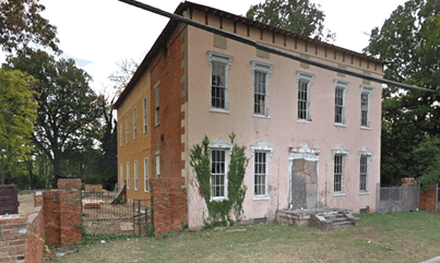 A historic two-story building with signs of wear, located on a grassy plot surrounded by trees, representing Memphis Heritage's efforts in preservation.