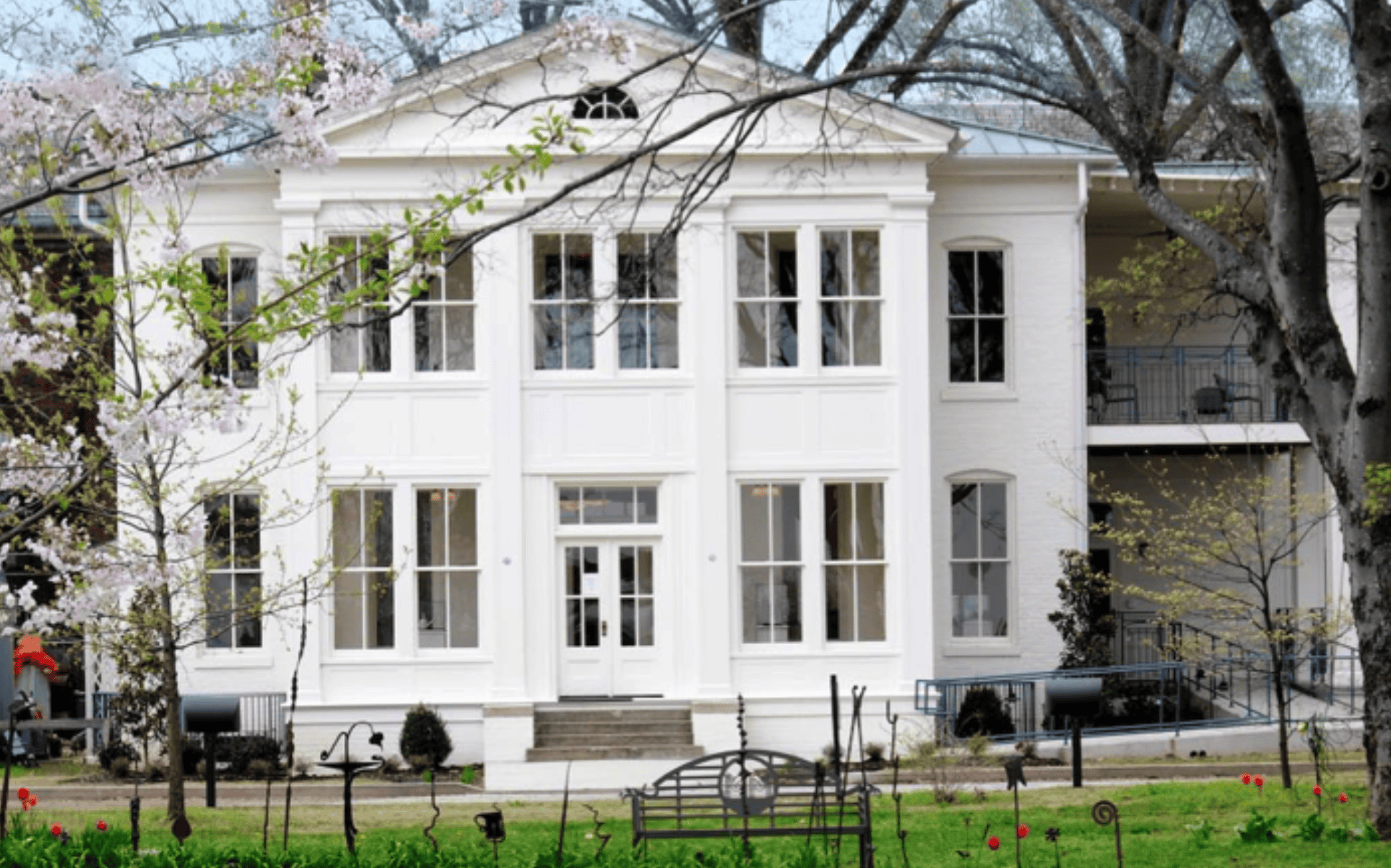 White historic house with large windows surrounded by blooming trees in Memphis, showcasing Memphis Heritage Inc.'s dedication to preserving local architecture and culture.